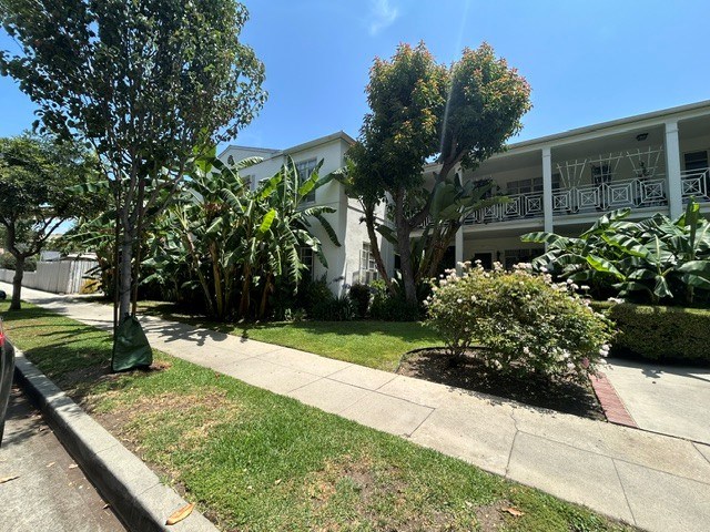 A white building with a balcony is surrounded by greenery.